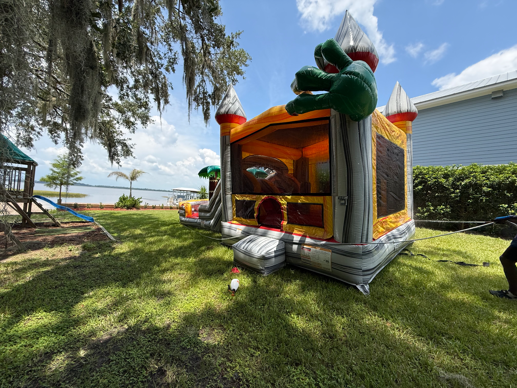 Dino bounce house with orange mesh enclosure and green dinosaur on a shaded lawn